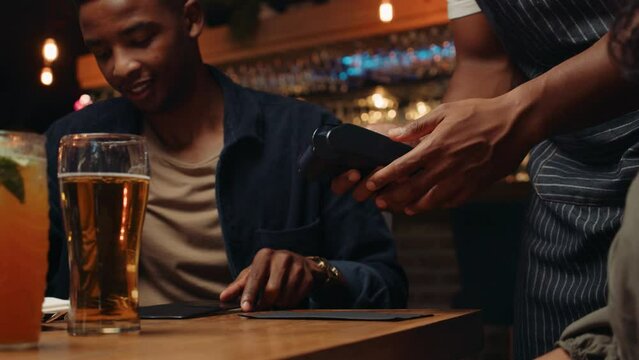 African American male tapping cellular device on card machine paying for dinner