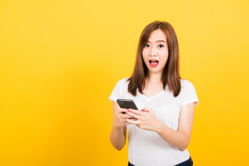 Fototapeta premium Asian happy portrait beautiful cute young woman teen smiling standing her surprised excited with smart mobile phone looking the phone isolated, studio shot yellow background with copy space