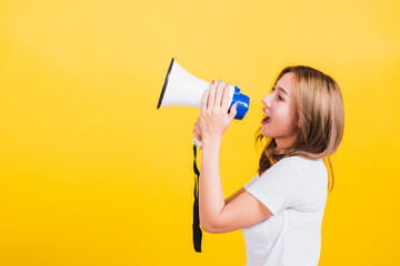 Asian Thai happy portrait beautiful cute young woman stand to make announcement message shouting screaming in megaphone looking to side away, studio shot isolated on yellow background with copy space