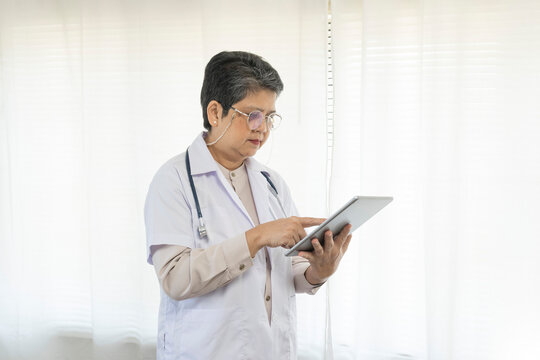 Serious senior female doctor using tablet computer standing in clinic.