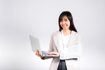 Asian business woman confident smiling broken arm after accident and wear arm splint for treatment but still have to work she hold laptop computer studio isolated on white background,copy space