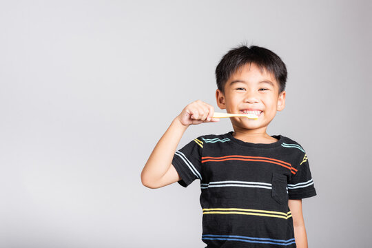 Little cute kid boy 5-6 years old brushing teeth and smile in studio shot isolated on white background, happy Asian children holding toothbrush in mouth by himself, Dental hygiene healthy concept