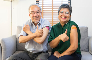 Senior Asian couple get vaccinated with bandage on arm show thumb up sign in living room. Grandfather and grandmother get vaccine.