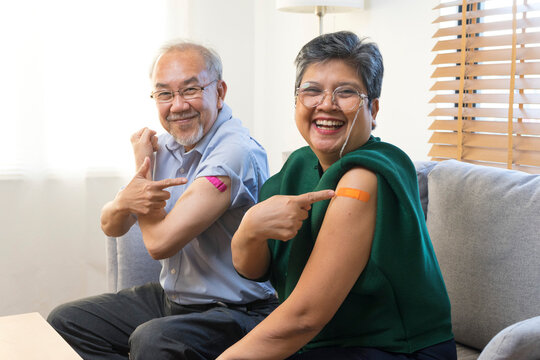 Senior Asian couple get vaccinated with bandage on arm show thumb up sign in living room. Grandfather and grandmother get vaccine. - Powered by Adobe