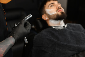 Professional hairdresser working with bearded client in barbershop, closeup