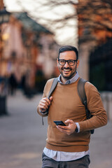 Portrait of happy caucasian man with glasses, holding his phone, sightseeing.