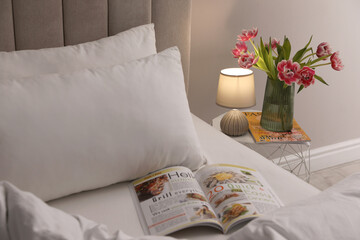 Stylish lamp, flowers and magazine on bedside table indoors. Bedroom interior elements