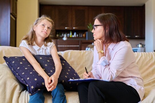 Woman Social Worker Talking To Girl Child At Home, Making Notes On Clipboard.