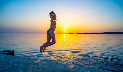 Girl jumping from pier in the water at sunset.