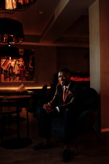 Portrait of a smiling handsome African American business man. Attractive charming man looks at the camera, smiles, sits on the couch. A young guy in a stylish suit looks at the camera with a smile.