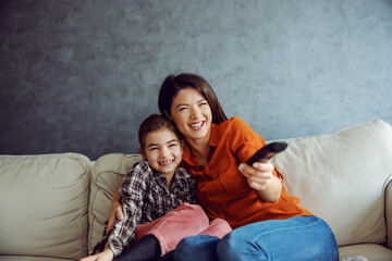 Smiling mother and daughter sitting on the sofa and watching family comedy. 