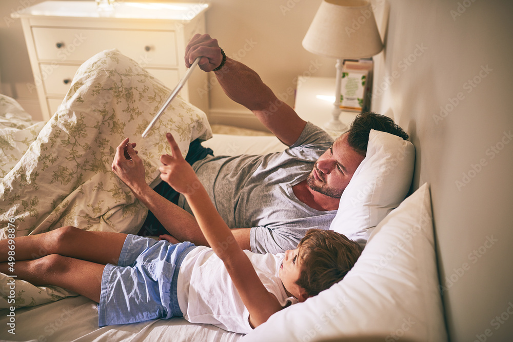 Poster Lets watch that next. Shot of a father and his little son using a digital tablet while lying in bed at home.