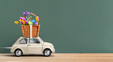 White car carrying basket with easter eggs and spring flowers atop on a green background.