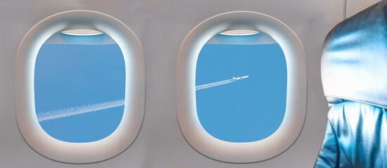 Trail of white smoke from the airplane on blue sky as seen through window of an aircraft