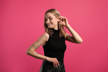 Beautiful woman with tattoos on arms against pink background