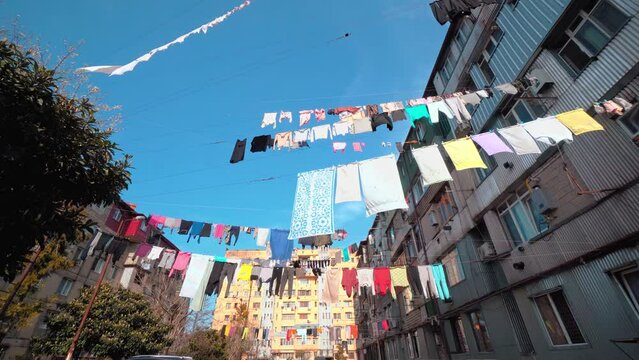 colorful linen hung in courtyard of an old vintage multi-storey building. wind develops them against background of blue sky. Georgia old favela district. Abandoned houses are people living in poverty