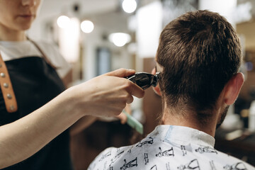 a hairdresser cuts a young guy with a hair trimmer, combing the hair on his head. Work of the...
