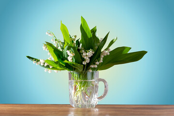 beautiful bouquet of fresh lilies of the valley in a glass mug on a wooden table