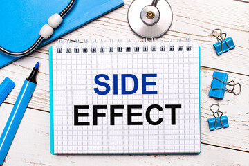 On a light wooden background, a stethoscope, a blue notepad, blue paper clips, a blue marker and a...