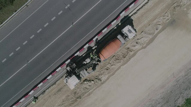 Aerial top down shot of a team of construction contractors hard at work on the side of a busy urban road a large concrete mixing truck unloading fresh material for the workers to prepare Galicia Spain
