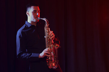 Young man playing saxophone on dark background. Space for text