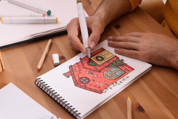 Man drawing in sketchbook with felt tip pen at wooden table, closeup