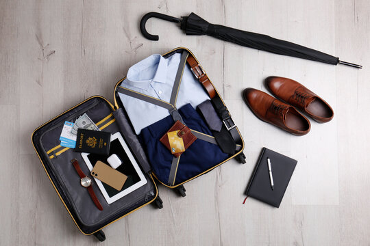 Packed suitcase with business trip stuff on wooden surface, flat lay