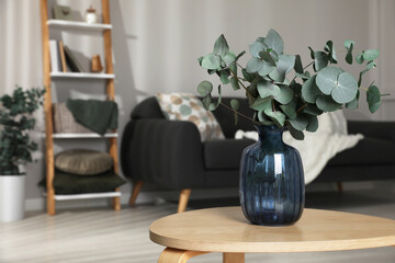Blue glass vase with beautiful eucalyptus branches on wooden table in living room, space for text