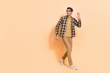 Full length body size view of attractive cheerful guy walking waving hi hello copy space isolated over beige pastel color background © deagreez