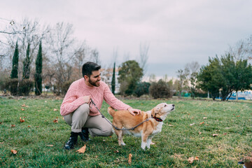 Happy young man crouched petting his dog walking in park