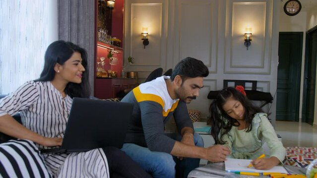 A pretty Indian housewife in casual clothes using a laptop in the living room - a businesswoman  nuclear family. A loving dad and his young daughter drawing a beautiful sketch together - artwork  s...