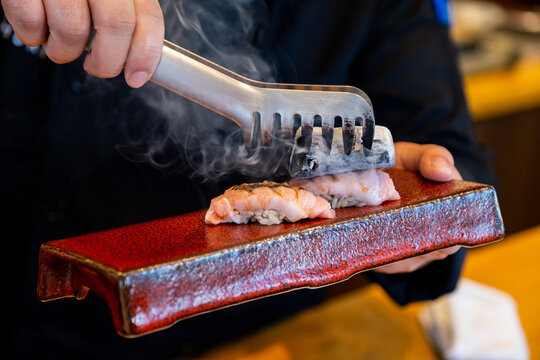 Close-up Professional sushi chef hand using Binchotan charcoal to aburi or flame seared otoro ( Tuna belly part ) to make perfect sushi with precision and confident.