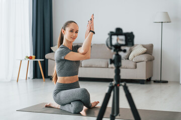 Fototapeta na wymiar Doing lessons on camera. Young woman with slim body type and in yoga clothes is at home