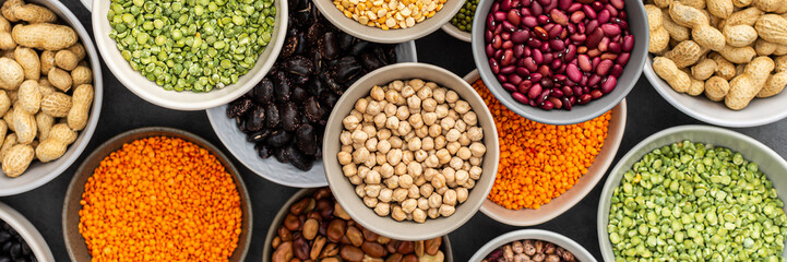 Banner of different types of legumes in bowls, green with yellow peas and mung beans, chickpeas and peanuts, colored beans and lentils, top view