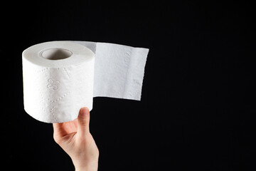 A roll of white soft toilet paper in a man's hand on a black background with space for text