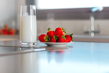 Glass of milk and plate with pile of fresh strawberries set on the table.