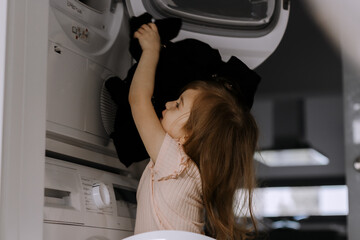 Cute toddler girl helping with general cleaning, puting clothes to drier.