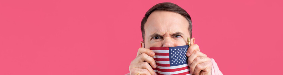 Portrait of a satisfied young man with a beard with an American flag on a red studio background. Great US patriot and defender of freedom.