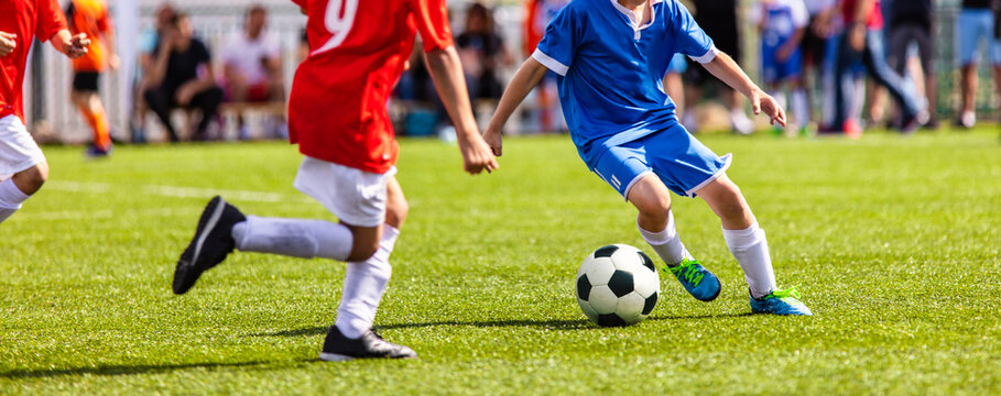 Boys play soccer. Teenagers playing soccer in sports field. Children kicking soccer game outdoors. Young male footballers running in red and blue sports uniforms