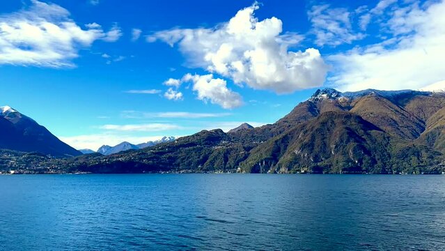 Time-lapse shooting of landscape on lake Como with sky and clouds against background of mountains.