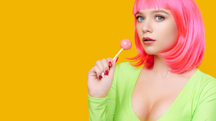 Young seductive woman on pink wig eat or lick big lollipop on bright yellow background