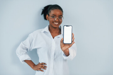 Holding smartphone. Young african american woman is against white background