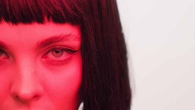 Portrait of a girl in red light with black lips and a wig on a white background in the studio. Woman in neon creative light.