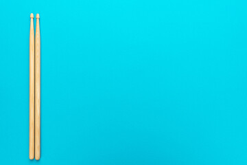 Minimalist photo of pair of wooden drumsticks on turquoise blue background. Flat lay top-down composition of drumsticks with copy space. Classic medium-sized 5B drumsticks.