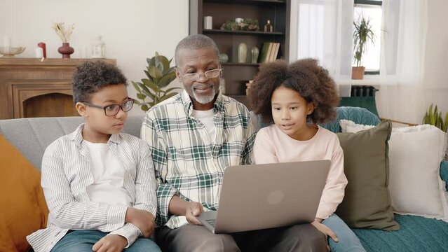 Happy african american grandfather and grandchildren choosing film on laptop app, spending weekend together, free space