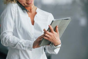 Tablet is in the hands. Woman with curly blonde hair is in autosalon