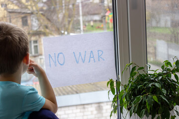 a little boy is holding a piece of paper on which is written no to war.