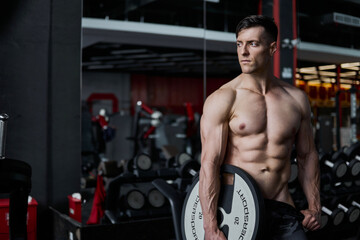 Fototapeta na wymiar Bodybuilder with heavy iron weight plate from barbell in sport gym.