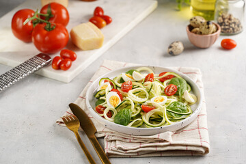 Keto paleo low-carb zoodles: zucchini noodles with parmesan cheese, cherry tomatoes, quil eggs on light grey surface