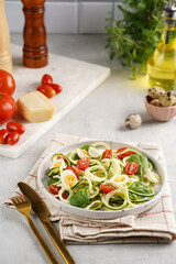 Keto paleo low-carb zoodles: zucchini noodles with parmesan cheese, cherry tomatoes, quil eggs on light grey surface